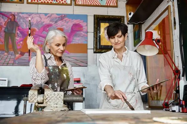Due donne, una coppia lesbica matura, esplorano uno studio d'arte con vivaci dipinti alle pareti. — Foto stock