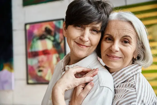 Two women hugging in front of paintings in an art studio. — Stock Photo