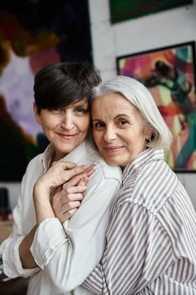 Two women hug in front of a painting in an art studio. — Stock Photo