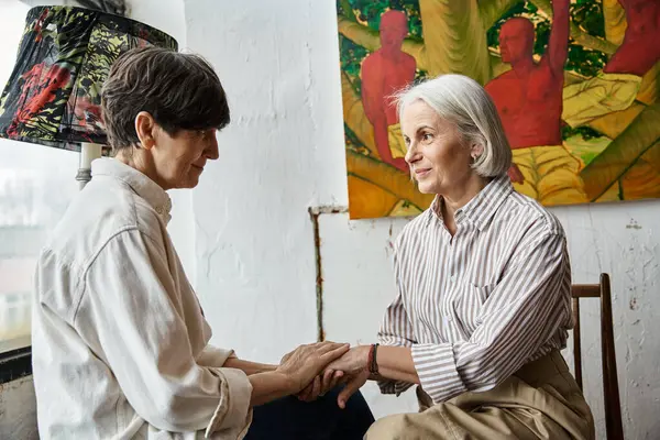 Mature lesbian couple admiring a painting together in art studio. — Stock Photo