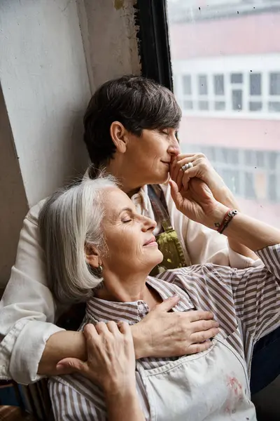 Lesbian couple enjoying peaceful moment by window in art studio. — Stock Photo