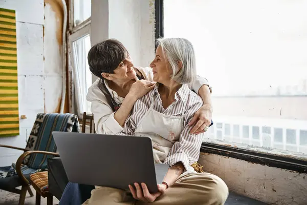 Couple on window sill engrossed in laptop. — Stock Photo