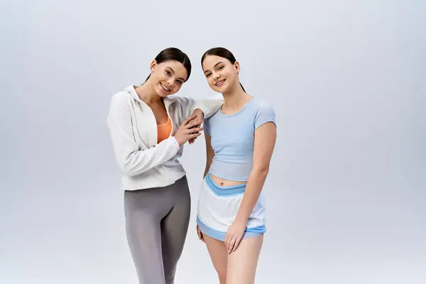 Duas meninas morenas bonitas e adolescentes em stand de trajes esportivos com braços ao redor um do outro, mostrando amizade e unidade. — Fotografia de Stock