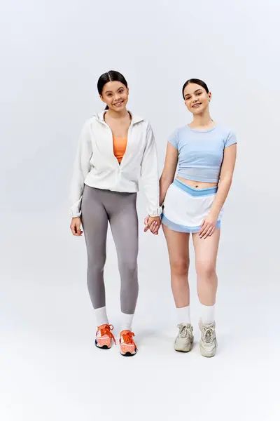 Due belle ragazze adolescenti brune stanno fianco a fianco, tenendosi per mano in una dimostrazione di amicizia su uno sfondo grigio dello studio. — Foto stock