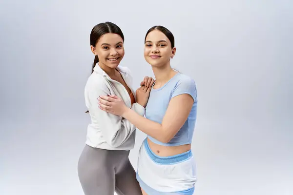 Deux jolies adolescentes sportives, une brune, posant en toute confiance ensemble dans un studio sur fond gris. — Photo de stock