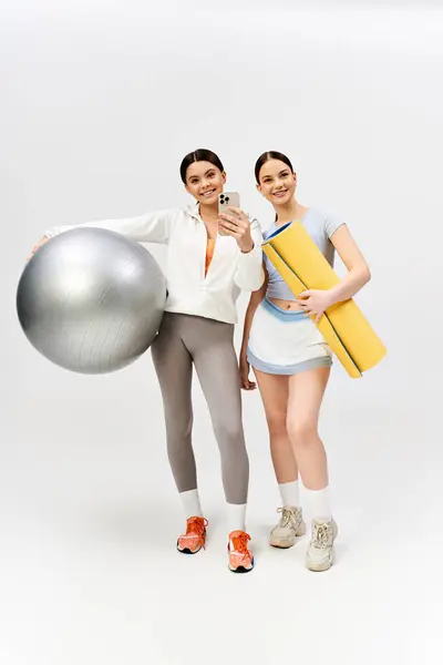 Dos chicas adolescentes guapas y morenas vestidas con atuendo deportivo se paran lado a lado en un estudio, mostrando su amistad. - foto de stock
