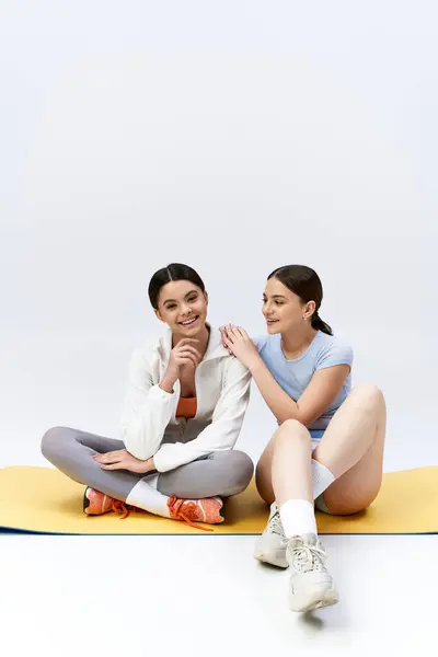 Две симпатичные брюнетки-девочки в спортивном наряде сидят на коврике, держась за руки в единстве и дружбе. — стоковое фото