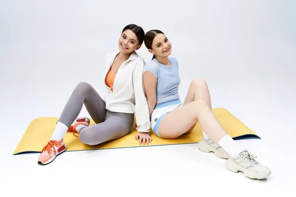 Дві красиві брюнетки-підлітки в спортивному вбранні сидять разом на килимку в студії, демонструючи дружбу і релаксацію. — стокове фото