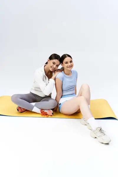 Дві молоді жінки в спортивному вбранні сидять на килимку для йоги, беручи участь у розслаблюючій сесії йоги в студії. — стокове фото