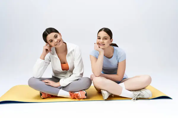 Дві дівчини-підлітки, красиві та брюнетки, сидять на килимку для йоги в студії. Вони посміхаються і позують на картину. — стокове фото