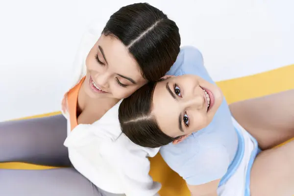 Дві красиві брюнетки дівчата-підлітки в спортивному вбранні сидять поруч один з одним на сірому фоні в студії. — стокове фото