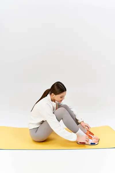Une jolie adolescente brune en tenue de sport s'assoit les jambes croisées sur un tapis jaune dans un studio. — Photo de stock