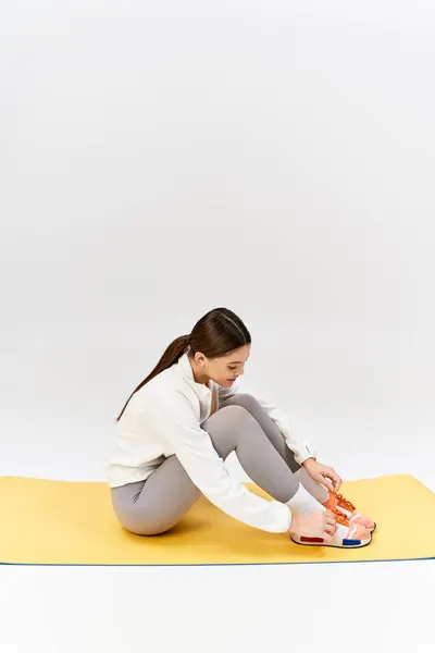 A pretty, brunette teenage girl in sportswear sits cross-legged on a yellow mat in a studio. — Stock Photo