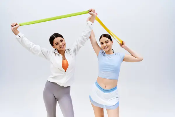Two pretty, brunette teenage girls in sportive attire stand together on a grey background in a studio. — Stock Photo