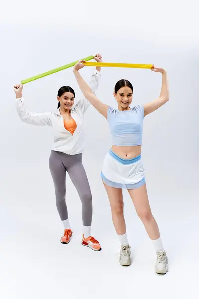 Due belle adolescenti brune in abbigliamento sportivo, in piedi insieme in uno studio su uno sfondo grigio. — Foto stock