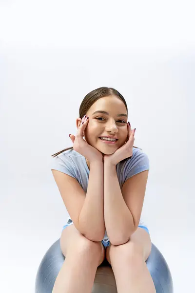 Ein hübsches, brünettes Teenager-Mädchen in sportlicher Kleidung sitzt anmutig auf einem Ball — Stockfoto