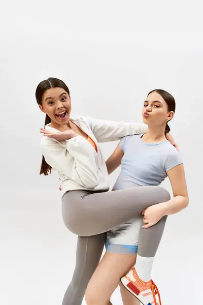 Two pretty, brunette teenage girls in sportive attire, posing in a studio against a grey background. — Stock Photo