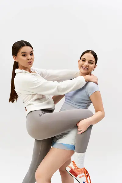 Дві красиві, спортивні дівчата-підлітки, одягнені в спортивний одяг позують разом у студії на сірому фоні. — стокове фото