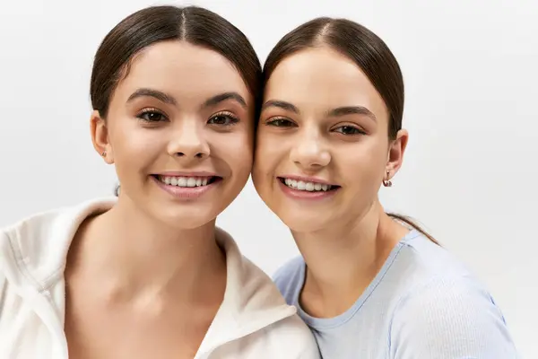 Zwei hübsche, sportliche und brünette Teenager posieren gemeinsam auf grauem Studiohintergrund und strahlen Selbstbewusstsein und Kameradschaft aus.. — Stockfoto