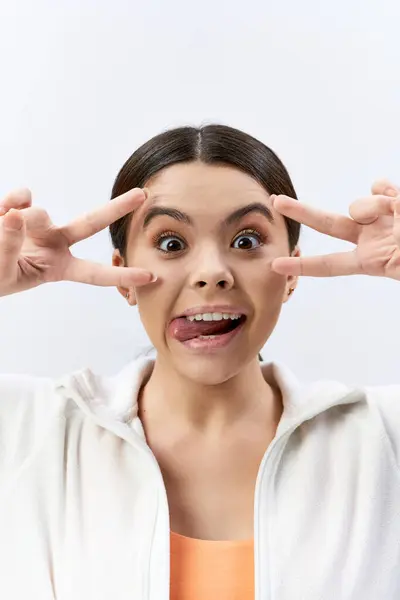 A brunette teenage girl in sportive attire playfully makes a funny face using her hands. — Stock Photo