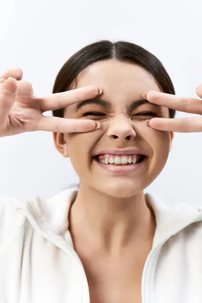 A brunette teenage girl in sportive attire playfully makes a face with her hands against a grey background in a studio. — Stock Photo
