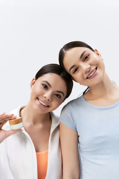 Дві красиві дівчата-підлітки, обидві з волоссям брюнетки, стоять разом посміхаючись яскраво в студії на сірому фоні. — стокове фото