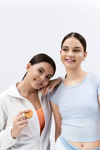 Two teenage best friends, brunette and pretty, stand side by side in sportive attire, smiling happily in a studio. — Stock Photo