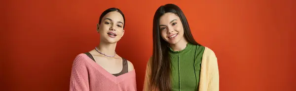 Two pretty and brunette teenage girls standing together in front of a vibrant red wall, showcasing friendship and unity. — Stock Photo
