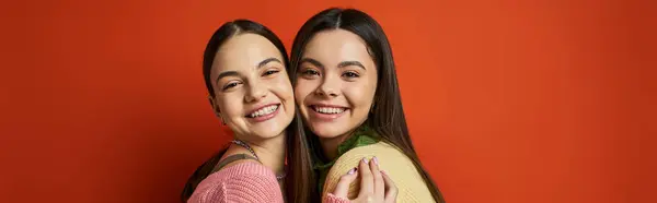 Дві молоді жінки, красива і брюнетка, обіймають один одного ласкаво перед яскравою червоною стіною. — стокове фото