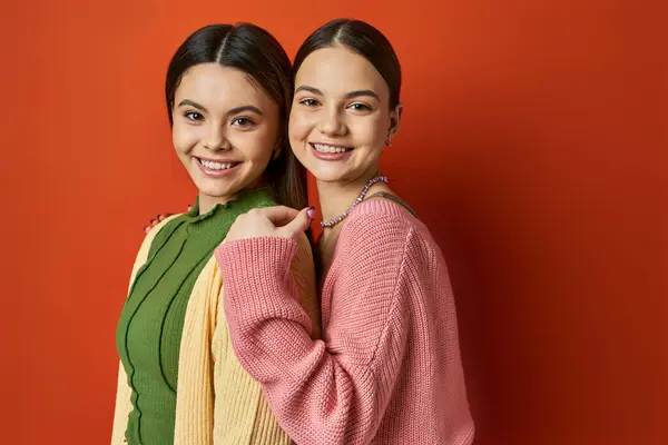 Дві красиві, повсякденні, брюнетки-підлітки стоять поруч перед яскраво-червоною стіною, символізуючи дружбу. — стокове фото