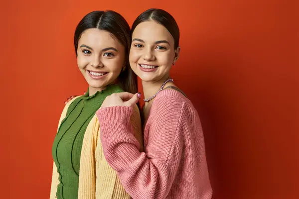 Two pretty, casual-clad, brunette teenage girls stand side by side in front of a vivid red wall, symbolizing friendship. — Stock Photo