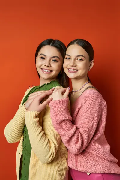Дві красиві і брюнетки дівчата-підлітки в повсякденному вбранні стоять пліч-о-пліч перед сміливою червоною стіною в студії. — стокове фото