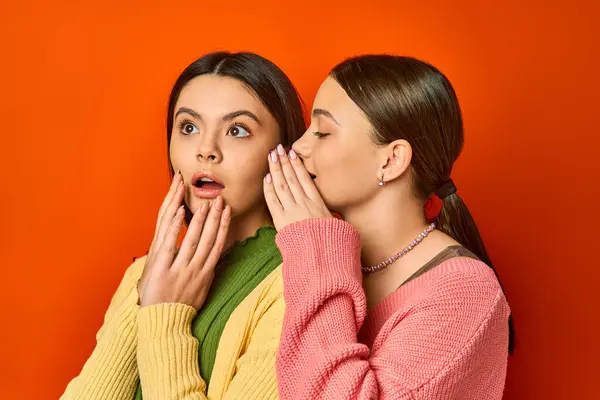 Due belle, bruna adolescenti in abbigliamento casual stand uno accanto all'altro con la bocca aperta a sorpresa su uno sfondo arancione studio. — Foto stock