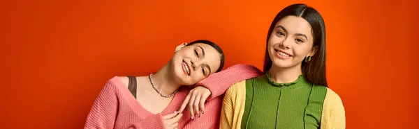 Deux jolies adolescentes brunes en tenue décontractée se tiennent étroitement ensemble sur un fond orange vif dans un studio. — Photo de stock