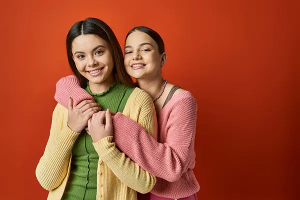 Zwei junge Frauen, eine hübsch und brünett, umarmen sich liebevoll vor einem leuchtend roten Hintergrund. — Stockfoto
