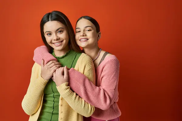 Two young women, one pretty and brunette, hugging affectionately in front of a vibrant red background. — Stock Photo