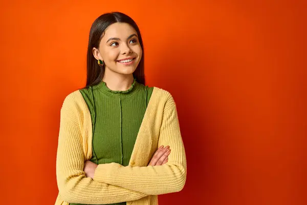 A brunette woman standing with arms crossed against an orange backdrop exuding confidence and poise. — Stock Photo