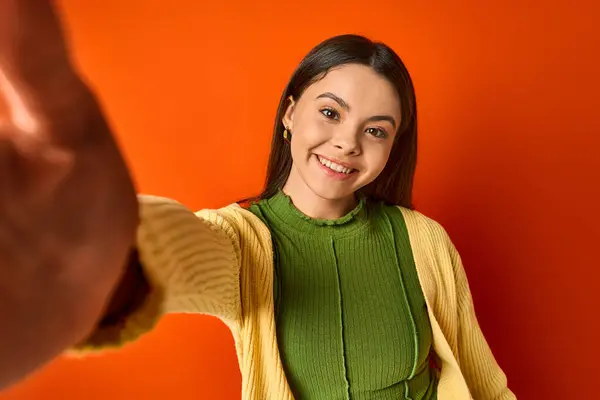 Une adolescente brune dans un pull vert et jaune pointe énergiquement vers quelque chose hors écran, dans un cadre de studio. — Photo de stock