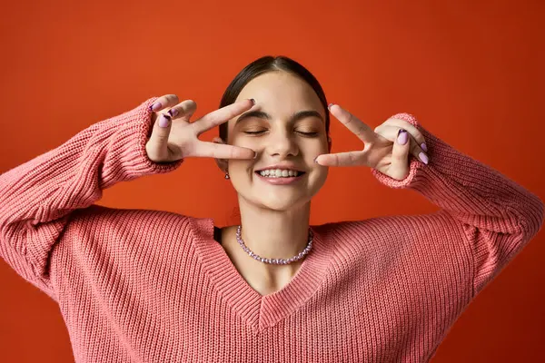 Une adolescente brune en tenue décontractée sourit tout en faisant un signe de paix avec ses mains, symbolisant l'unité et l'harmonie. — Photo de stock