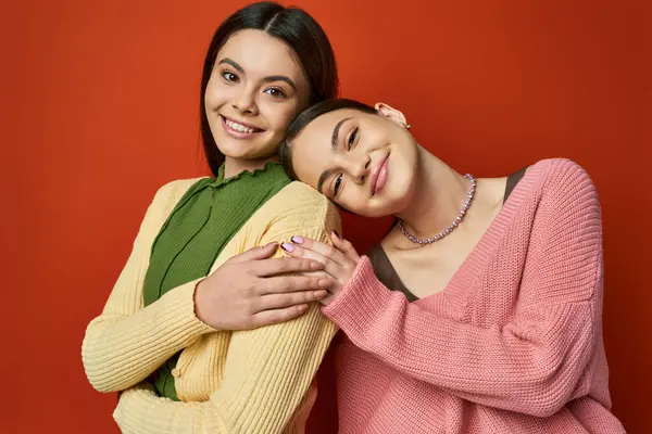 Duas meninas adolescentes morena bonita, amigos do sexo feminino, ficar lado a lado em traje casual em um fundo estúdio laranja. — Fotografia de Stock