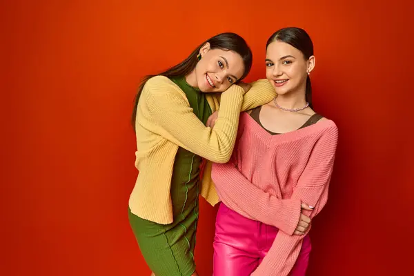 Zwei hübsche Brünetten, Teenager-Freunde, stehen zusammen vor einer leuchtend roten Wand in einem Studio-Setting. — Stockfoto
