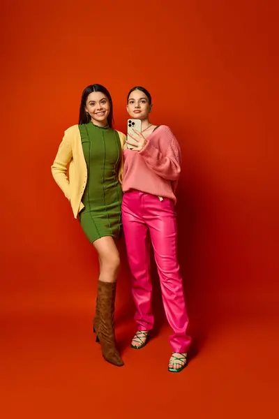 Dos guapas morenas adolescentes con atuendo casual se paran juntas frente a un vibrante fondo rojo. - foto de stock