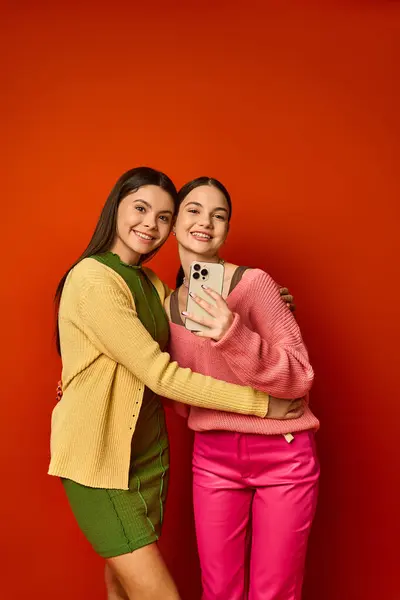 Дві красиві дівчата-підлітки, брюнетка і випадково одягнені, стоять поруч перед яскравою червоною стіною. — стокове фото