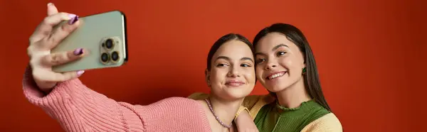 Дві молоді жінки, друзі, беручи селфі зі смартфоном на помаранчевому фоні в студійній обстановці. — стокове фото
