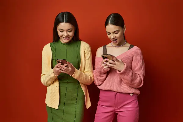 Zwei hübsche, brünette Teenager-Mädchen stehen zusammen, in ihre Handys vertieft und ignorieren ihre Umgebung. — Stockfoto