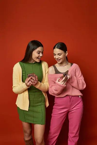 Zwei hübsche, brünette Teenager-Mädchen stehen nebeneinander und strahlen Freundschaft und Kameradschaft vor einem leuchtend orangefarbenen Hintergrund aus.. — Stockfoto