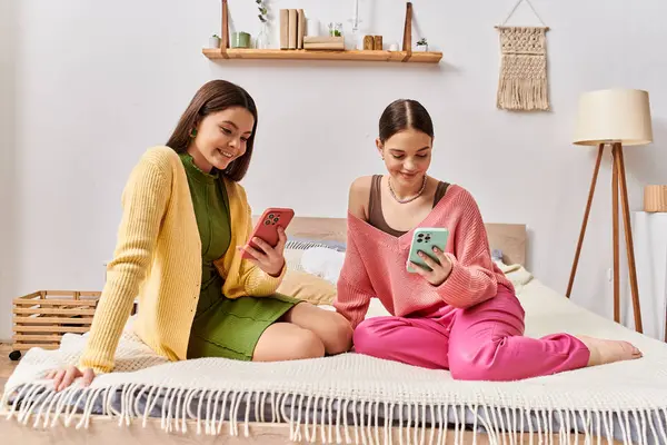 Deux adolescentes en tenue décontractée assises sur un lit, absorbées dans leurs téléphones cellulaires. — Photo de stock