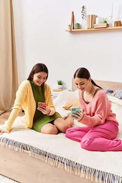 Deux jolies adolescentes en tenue décontractée s'assoient sur un lit, absorbées dans un livre, profitant d'un moment paisible ensemble. — Photo de stock