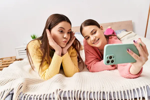 Дві красиві дівчата-підлітки в повсякденному вбранні лежать на ліжку, приймаючи селфі — стокове фото
