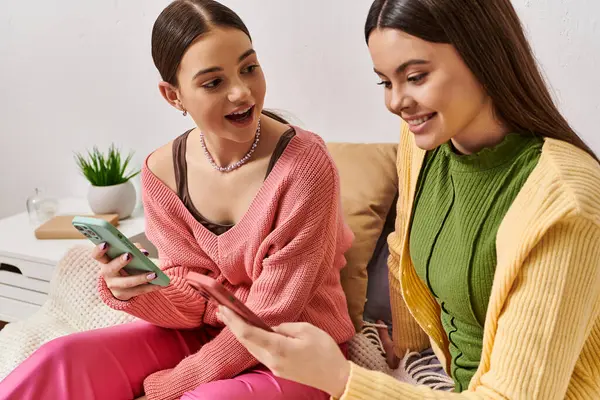 Two women in casual attire sit on a couch, engaged in conversation while looking at a cell phone. — Stock Photo